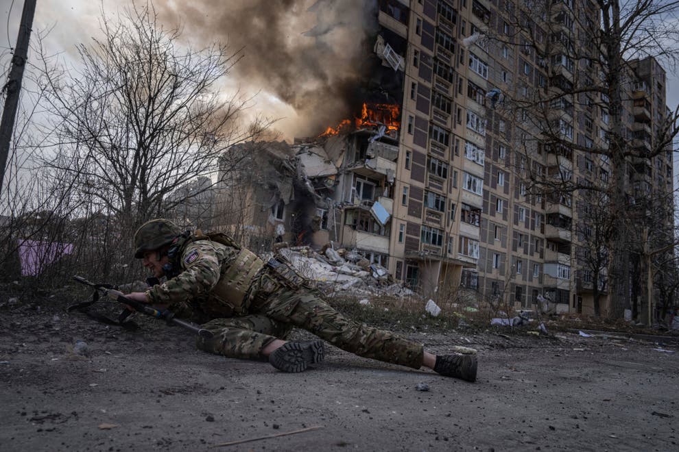 A Ukrainian police officer takes cover in front of a burning building that was hit in a Russian airstrike in Avdiivka